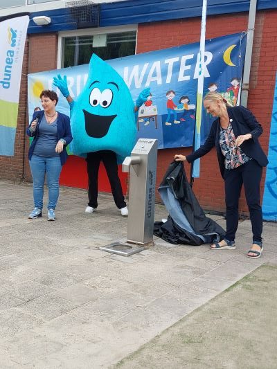 Bianca Heijsteeg (directeur OBS Erasmus), mascotte Druppie en Korrie Louwes (algemeen directeur OCW gemeente Den Haag) onthullen de watertap.