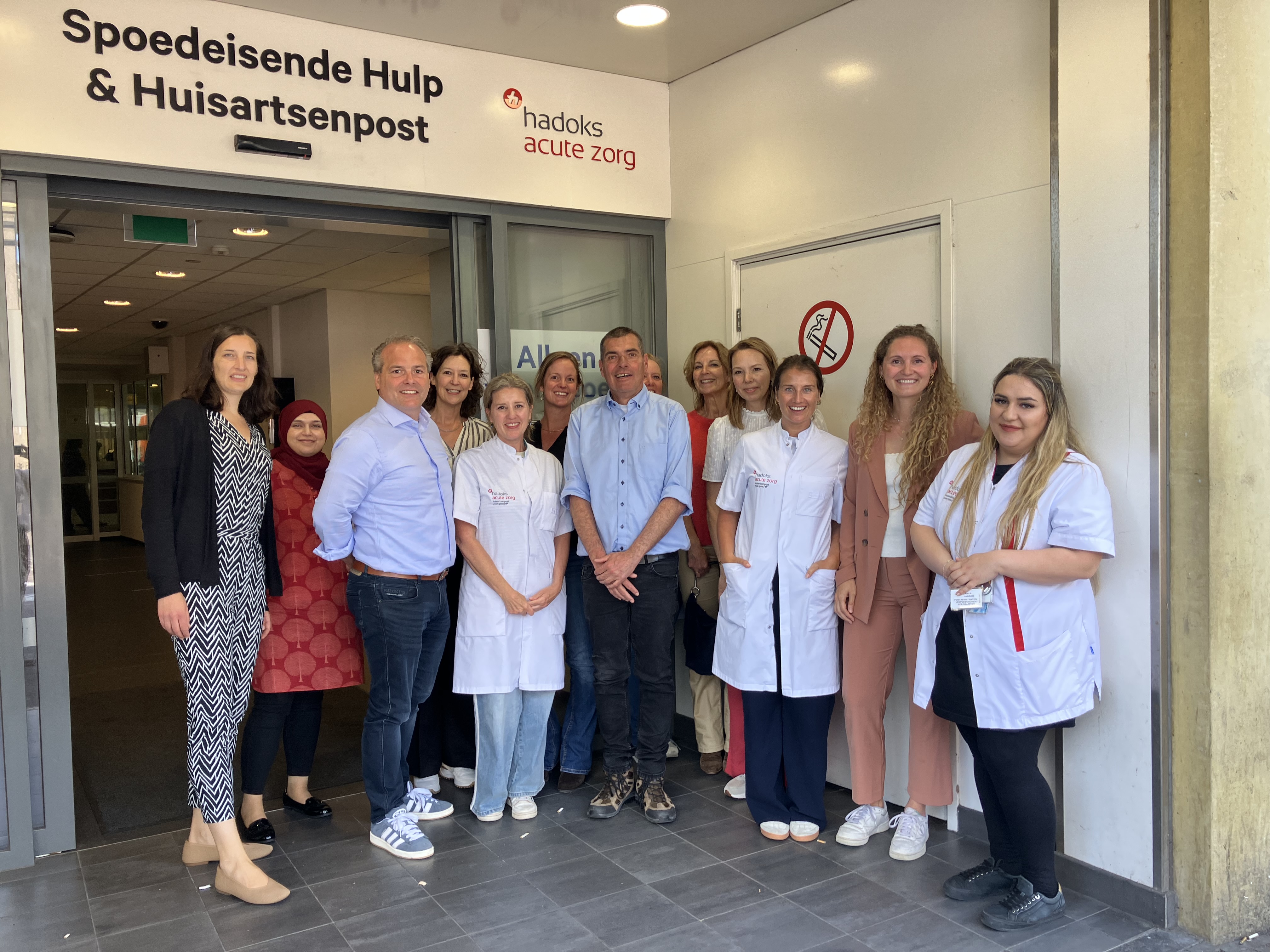 Medewerkers van Hadoks en de Meldkamer Ambulancezorg Haaglanden poseren voor de ingang van de Huisartsenspoedpost aan het Westeinde in Den Haag.