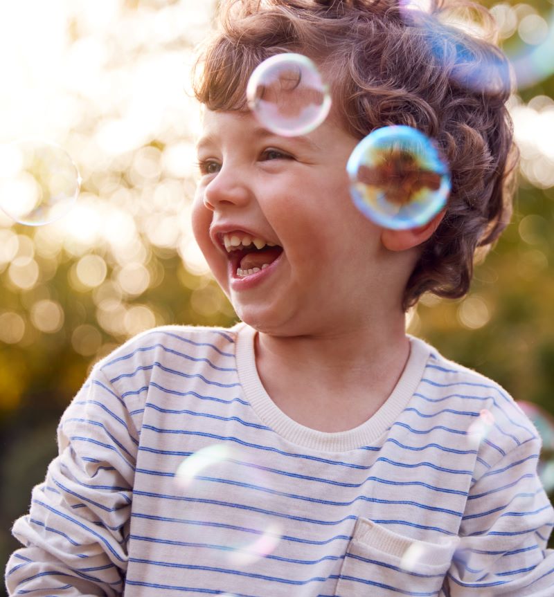 lachend jongetje van kleuterleeftijd in de buitenlucht. Om hem heen dwarrelen zeepbellen.