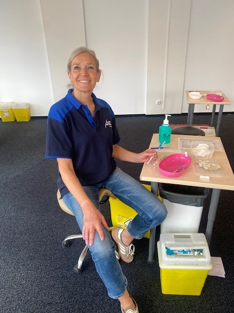 verpleegkundige Angelique kijkt lachend in de camera acher haar bureau bij de vaccinatielocatie.