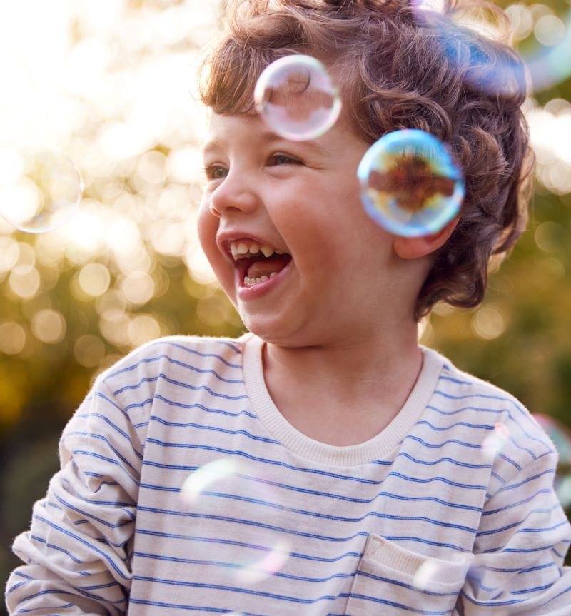 lachend jongetje van kleuterleeftijd in de buitenlucht. Om hem heen dwarrelen zeepbellen.