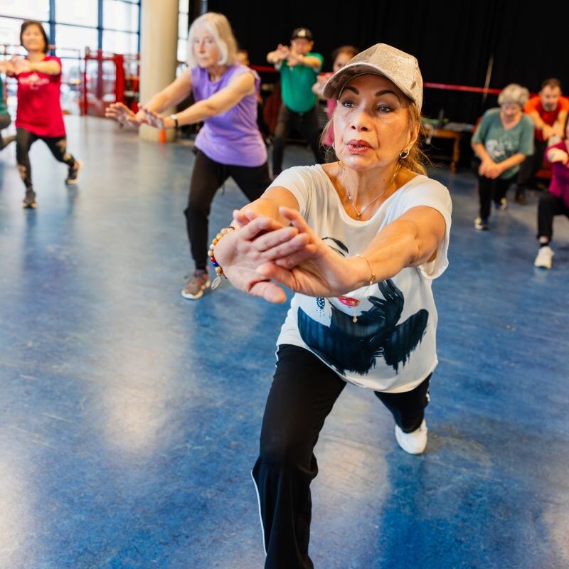 oudere dame bij aerobicles met op de achtergrond een aantal medecursisten
